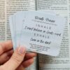 Hand holding breath praer cards set against an open Bible. The cards have simple, faith-based phrases for daily prayer and reflection.