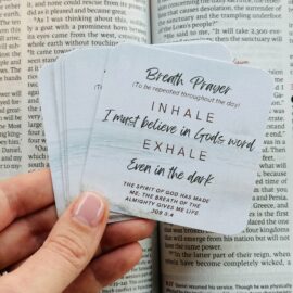 Hand holding breath praer cards set against an open Bible. The cards have simple, faith-based phrases for daily prayer and reflection.