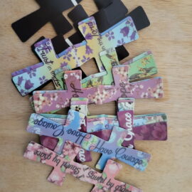 Decorative cross made of cut-out phrases and flowers on a wooden surface.