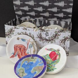 An open box with round ornaments inside and three ornaments leaning on the outside of the box.