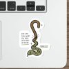 A die-cut sticker featuring a cartoon green and brown snake with the text 'GOD CAN TURN WHAT YOU DO INTO WHAT HE NEEDS' and 'EXODUS 4:2-4' on a white laptop palm rest, shown on a wooden desk next to a keyboard, mouse, and stylus.