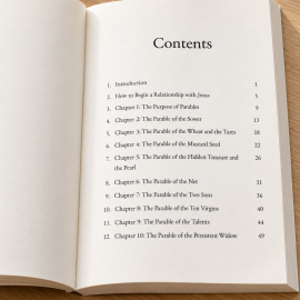 Open paperback of The Parables of Jesus displaying the table of contents on a light oak table with subtle greenery and a neutral pen.