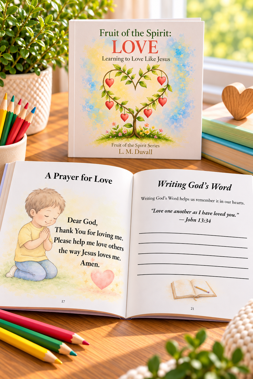 Fruit of the Spirit: LOVE – Learning to Love Like Jesus by L. M. Duvall, a Christian children's activity book for ages 4–7, displayed on a warm wooden tabletop with colored pencils and greenery. Open pages feature “A Prayer for Love,” illustrated with a praying child, and “Writing God's Word,” featuring John 13:34 and Scripture writing lines.