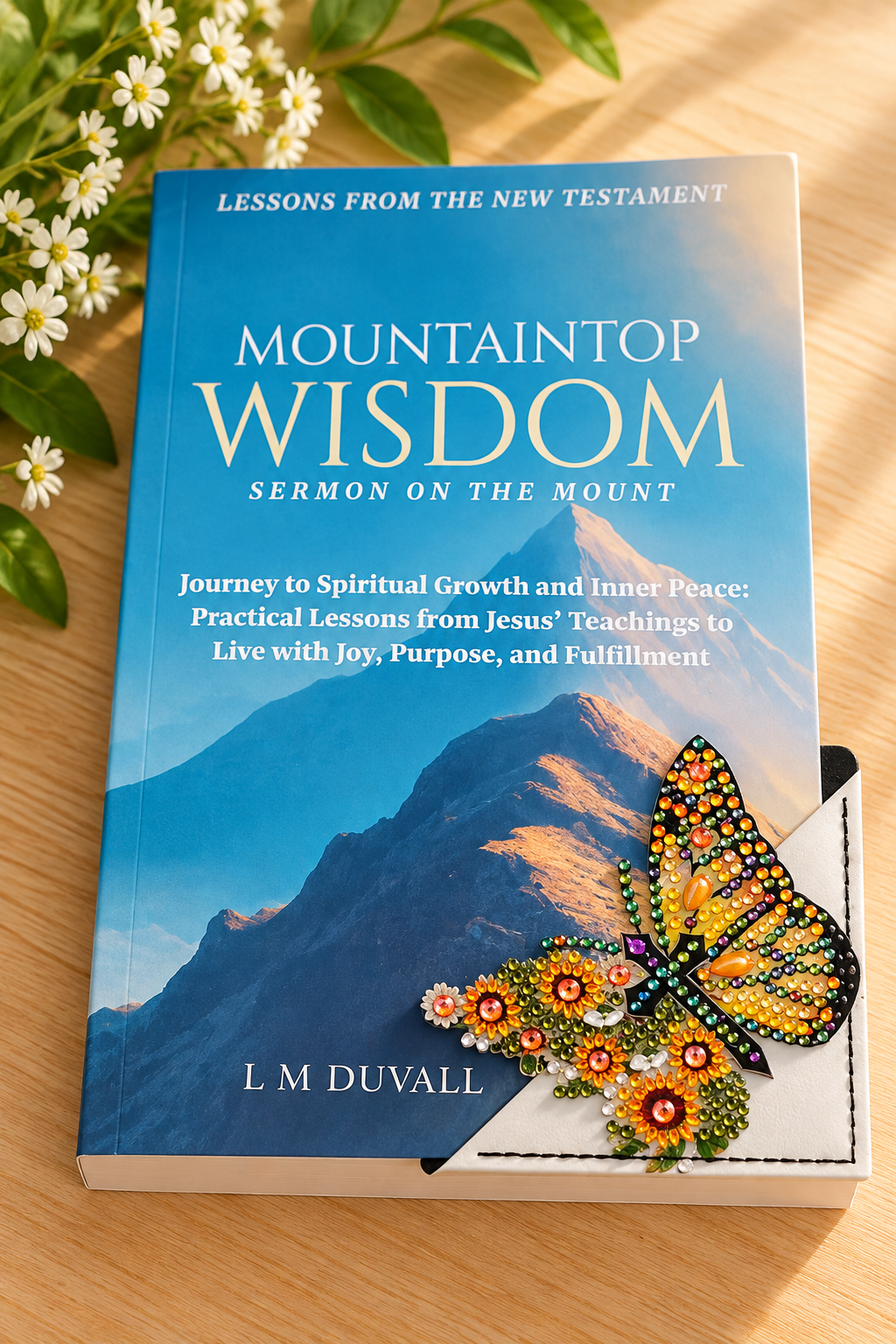 Colorful diamond art butterfly corner bookmark with sparkling floral details displayed on Mountaintop Wisdom: Sermon on the Mount by L. M. Duvall, resting on a light oak tabletop with soft greenery and white flowers.