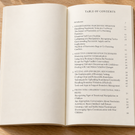 Open The Path to Peace paperback displaying the table of contents on a light oak table with subtle greenery and a neutral pen.